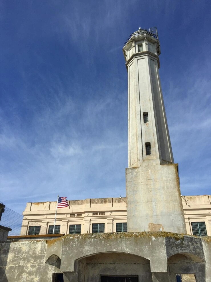 Alcatraz Island at sunset with prison buildings and an American flag in the foreground