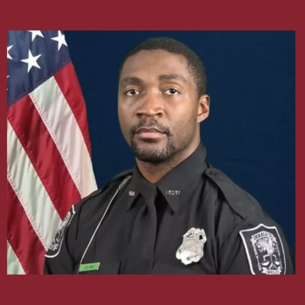 Police officers stand solemnly beside a memorial of flowers and an American flag, honoring fallen Officer David Rose near the CDC campus in Atlanta.