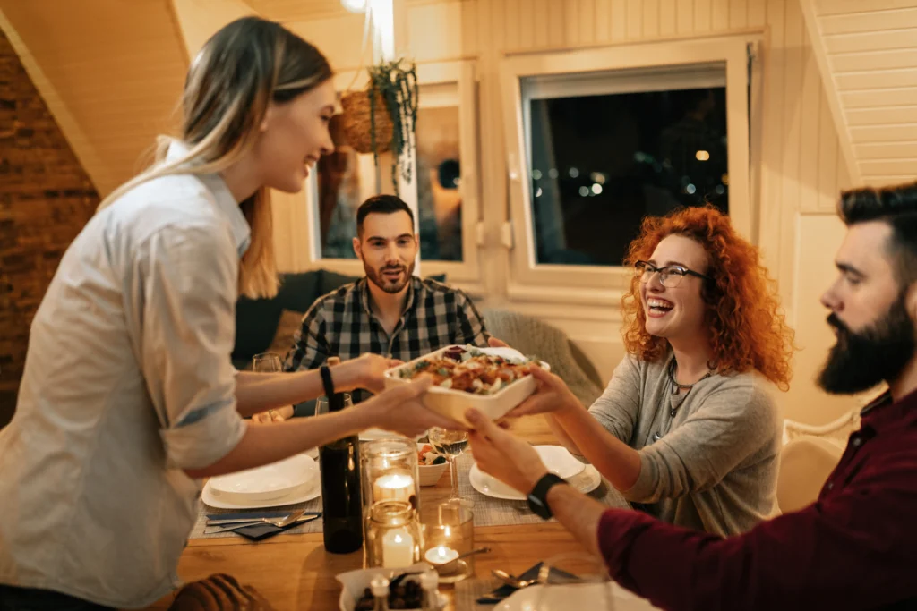 A beautifully decorated Friendsgiving table with autumn-themed decorations, cozy lighting, and a group of friends gathering for a festive meal.