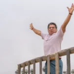 César Chávez portrait with a backdrop of protest signs and headlines highlighting the 2026 allegations, symbolizing a reevaluation of his legacy