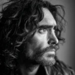 Russell Brand smiling at a public event, wearing a suit and glasses