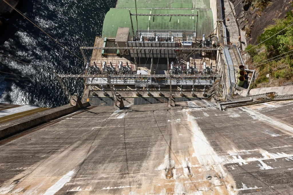 Panoramic view of the Three Gorges Dam spanning the Yangtze River in China with water flowing through massive spillways and surrounding mountains.