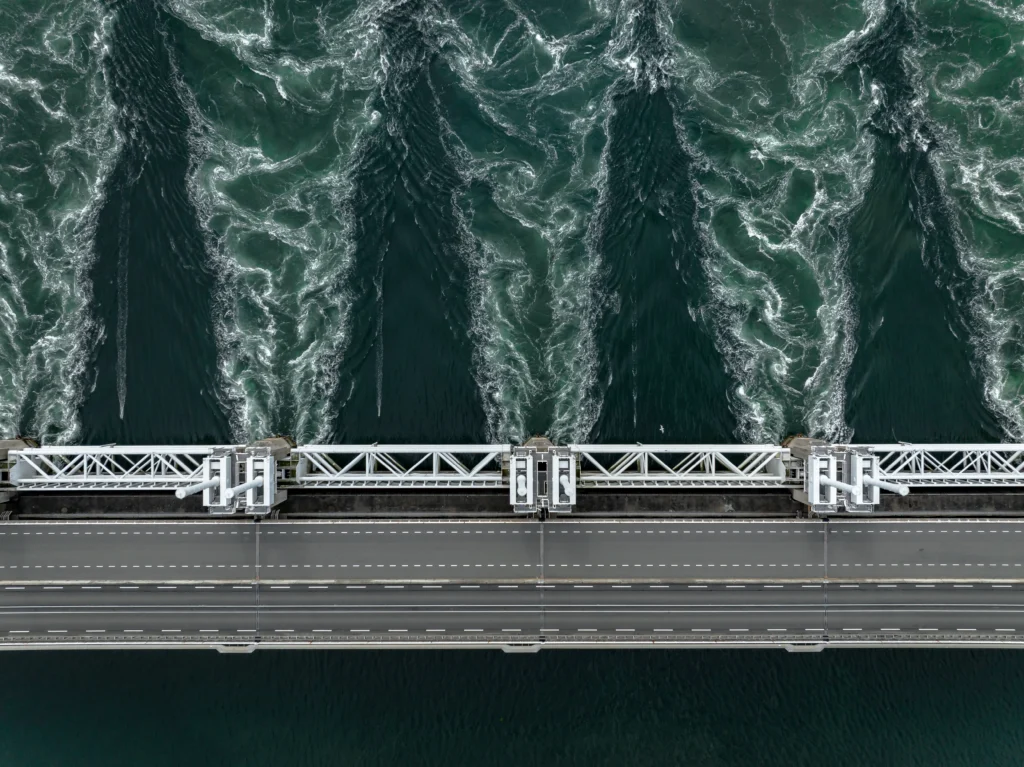 Panoramic view of the Three Gorges Dam spanning the Yangtze River in China with water flowing through massive spillways and surrounding mountains.