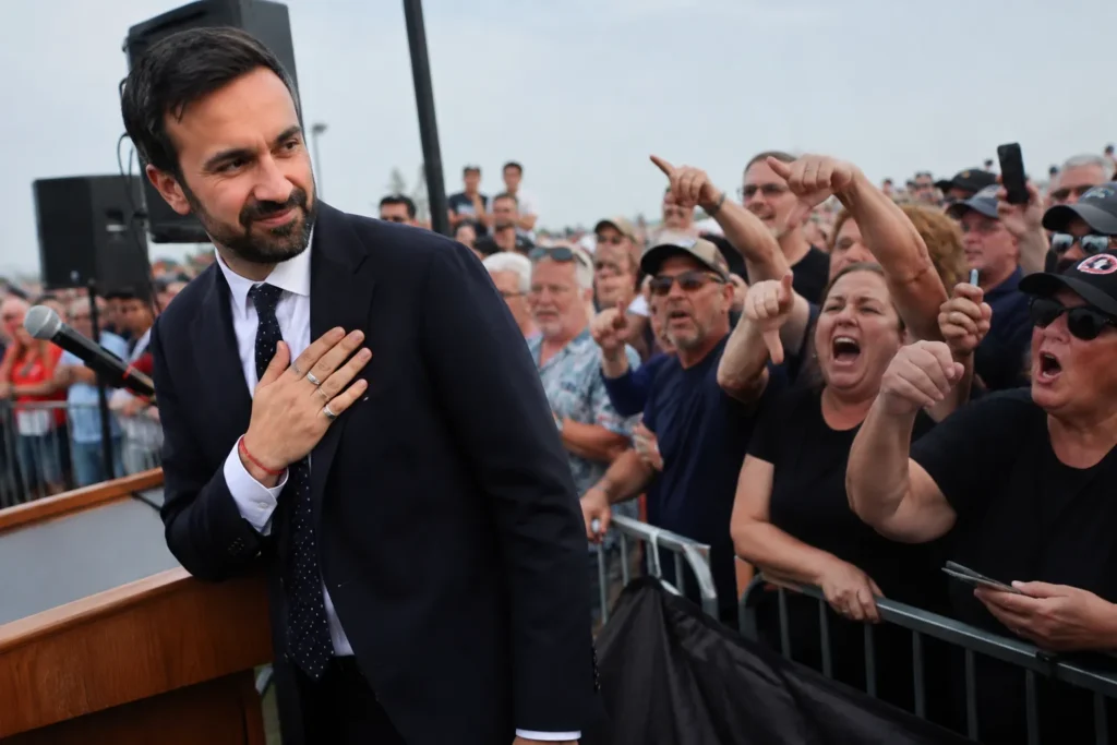 illustration of Zohran Mamdani standing near a podium as a crowd boos and gestures during an outdoor political event.