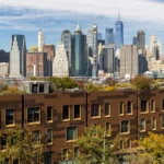 Affordable housing construction in New York with apartment buildings, cranes, and the Manhattan skyline in the background.